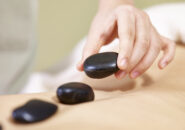 close-up of hand of a masseur placing stone on back of customer to perform hot stone massage.
